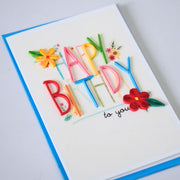 Angled view of colorful Happy Birthday quilled greeting card with raised lettering and paper flowers