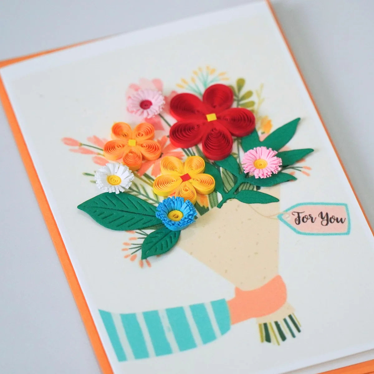 Angled view of for You quilled greeting card with a colorful paper flower bouquet held by an illustrated hand