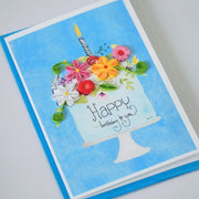 Angled view of happy Birthday Cake quilled greeting card with colorful paper flowers and a candle