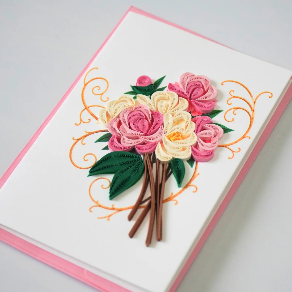 Side view showing coiled pink and ivory paper roses with dark green leaves