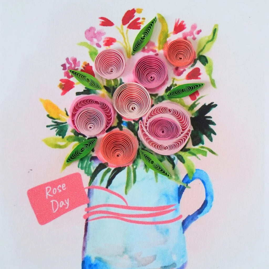 Detail of pink and peach coiled paper roses above a blue jug and Rose Day tag
