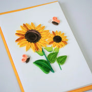 Angled view of sunflower and butterfly quilled greeting card with yellow paper flowers and green leaves